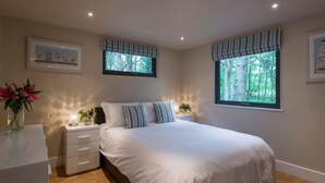 A bedroom with a large bed, two bedside tables, a nightstand, a dresser, and two windows with curtains. - Bracken Howe Lodge (Whitby)