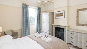 A bedroom with a bed, a dresser, a wardrobe, a fireplace, and a chandelier. - 12 St Hilda's (Whitby)