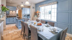 A kitchen with blue cabinets, a dining table set for four, and a window with a view of the outside. - 12 St Hilda's (Whitby)
