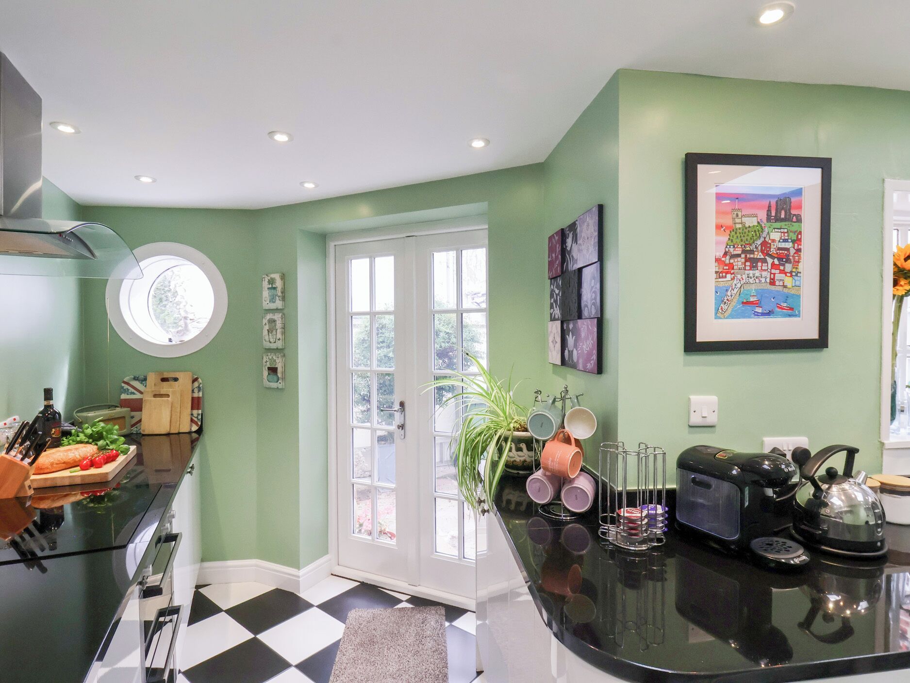 A kitchen with a checkered floor, a coffee machine, and a window with a view of greenery.