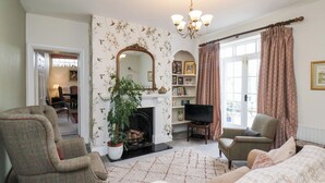 Ein Wohnzimmer mit Kamin, Fernseher und einem großen Fenster mit Vorhängen.