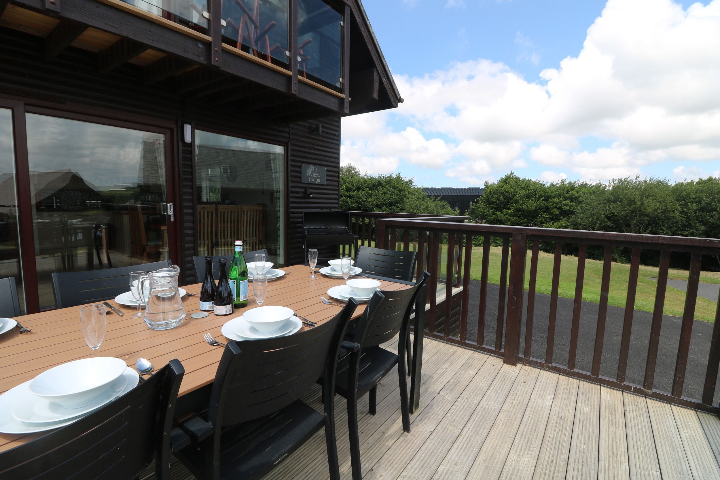 A wooden deck with a table set for dining, overlooking a grassy area.