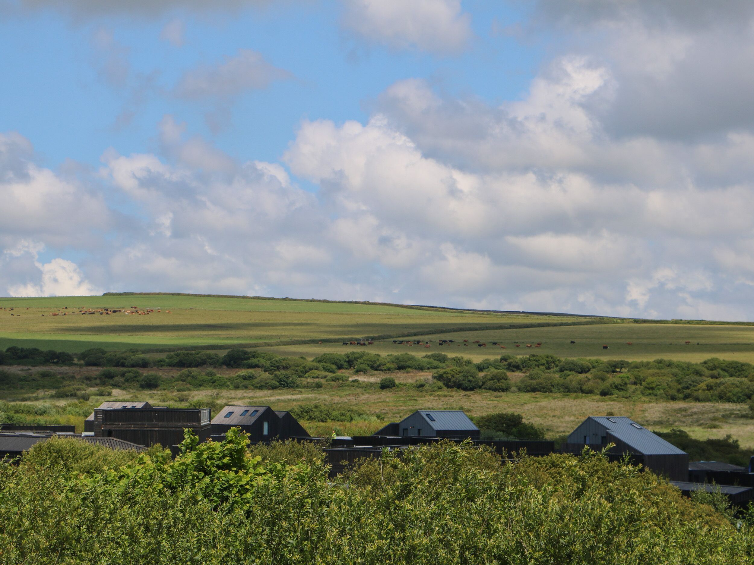 A rural landscape with rolling hills, a clear sky, and a few buildings in the foreground.