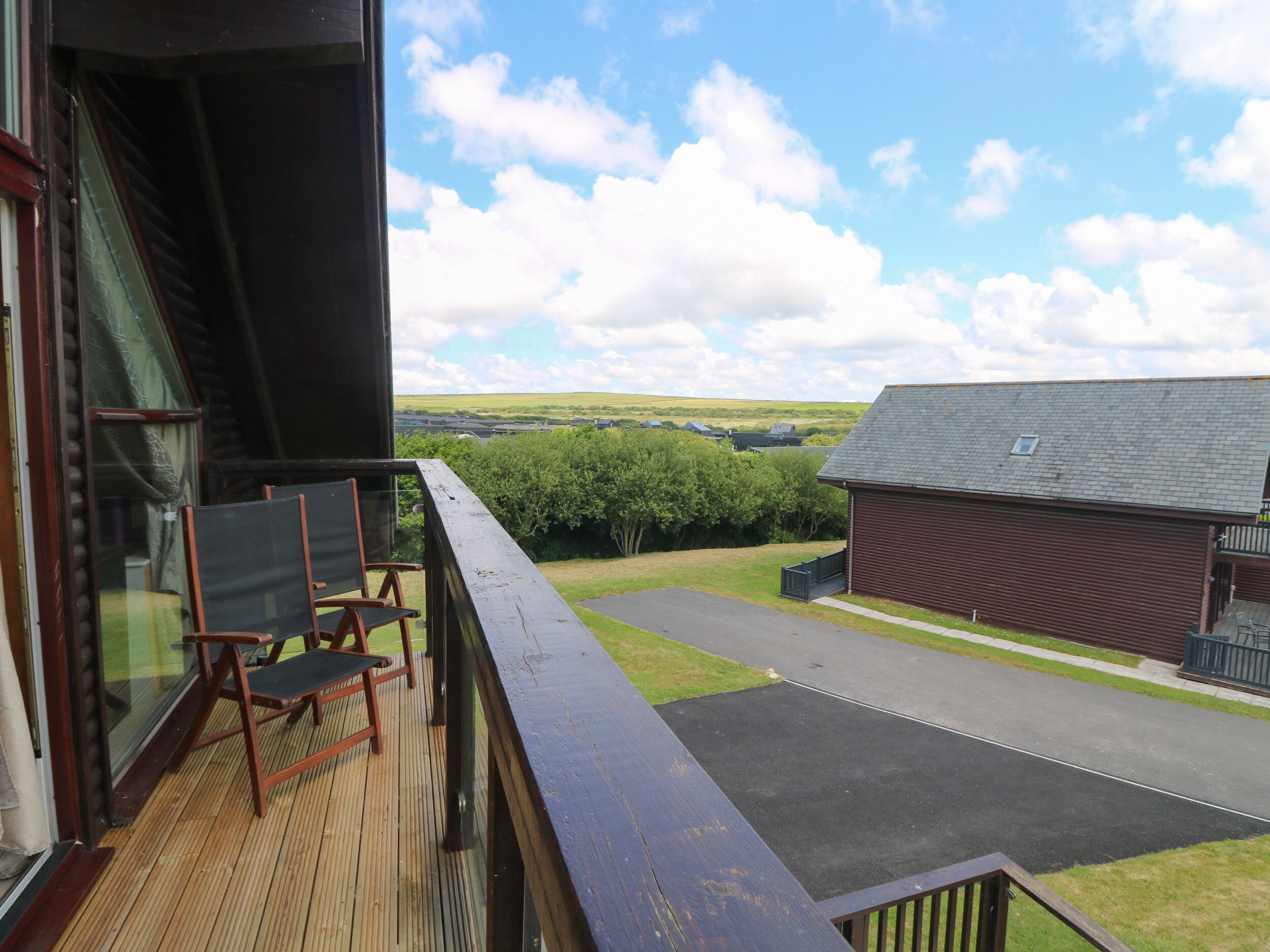 A wooden deck with chairs, a view of a rural landscape, and a barn.