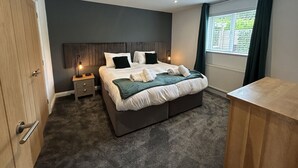 Une chambre à coucher moderne avec un grand lit, une table de chevet, une commode, une fenêtre avec des rideaux et une porte en bois.