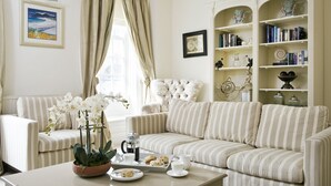 A living room with striped sofas, a coffee table with pastries, a bookshelf, and a window with curtains. - Albany House, Whitby (Whitby)