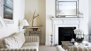 A living room with a fireplace, a sailboat model, a lamp, and a table with flowers and cookies. - Albany House, Whitby (Whitby)