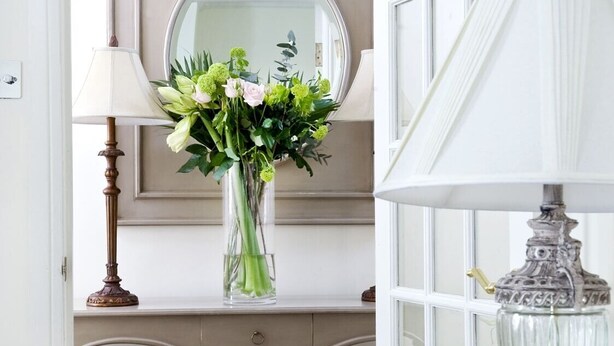 A room with a vanity, a mirror, a vase with flowers, a lamp, and a decorative glass container. - Albany House, Whitby (Whitby)