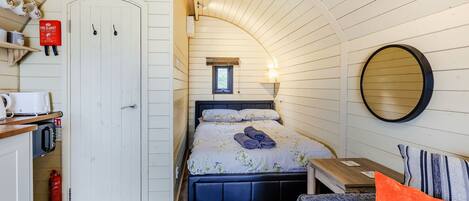 A cozy room with a bed, a small table, a chair, a round mirror, and a window.