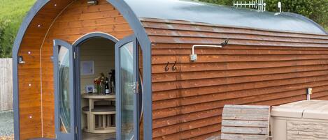 A cozy, wooden cabin with a curved roof, a glass door entrance, a small table, and a bench.
