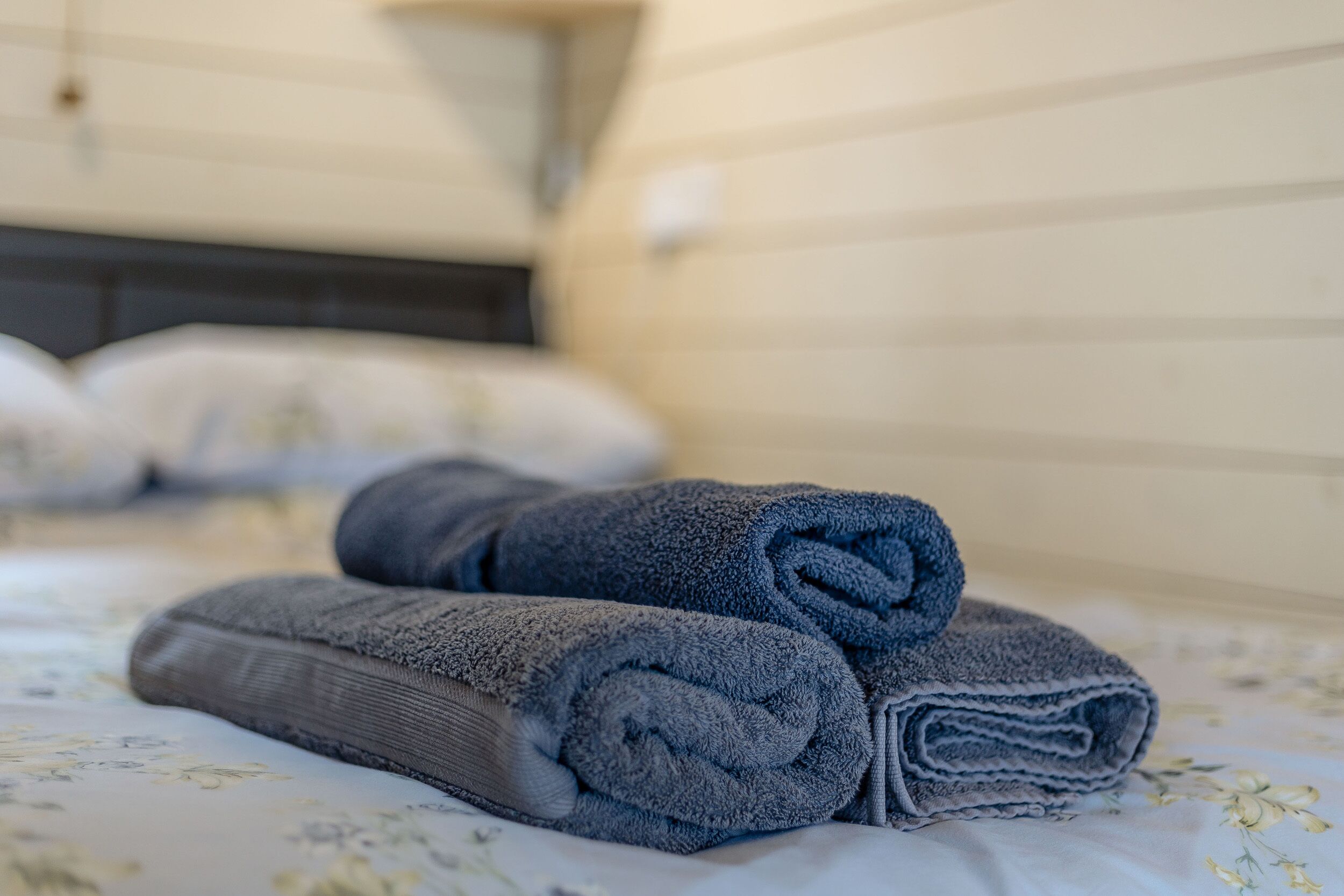 A neatly made bed with rolled towels and a floral-patterned bedspread.