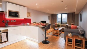 Um apartamento moderno com cozinha, área de refeições e sala de estar. Possui uma parede de destaque vermelha, piso de madeira e uma grande janela com cortinas.