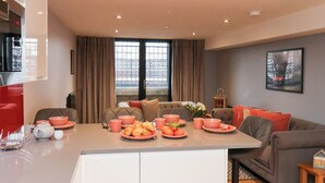 Uma sala de estar moderna com área de jantar, apresentando um conjunto de sofás, uma mesa de centro e bancada de cozinha com itens para o café da manhã.