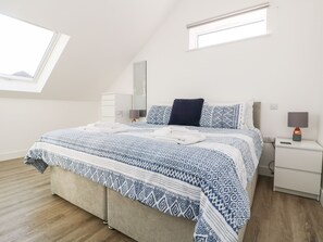 Relax in this serene bedroom with a large bed and sloped ceiling, featuring two skylights and a minimalist design.