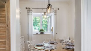 Een eetgedeelte met een houten tafel voor vier personen, witte stoelen en een raam met uitzicht op groen.