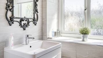 Un baño con un lavamanos blanco, un espejo con un marco ornamentado y una ventana con vidrio esmerilado.