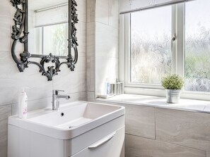 Ein Badezimmer mit einem weißen Waschbecken, einem Spiegel mit aufwendiger Rahmung und einem Fenster mit Milchglas.