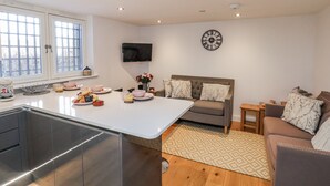 A modern kitchen with a central island, a dining area with a sofa, and a TV mounted on the wall. - George Stephenson @ Engine Shed (Whitby)