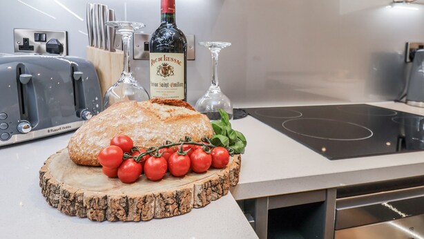 A kitchen counter with a loaf of bread, tomatoes, and a bottle of wine. - George Stephenson @ Engine Shed (Whitby)