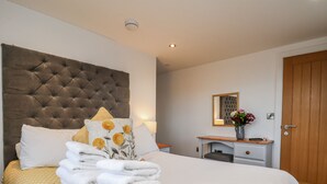 A neatly made bed with a tufted headboard, a bedside table with a lamp, and a wooden door. - George Stephenson @ Engine Shed (Whitby)