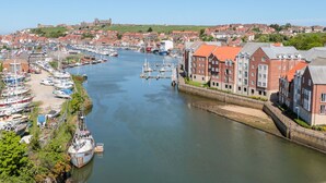 A harbor with boats, a bridge, and buildings along the river. - George Stephenson @ Engine Shed (Whitby)