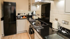 A modern kitchen with a black refrigerator, a stove, and a toaster. - Bay Cottage (Filey)