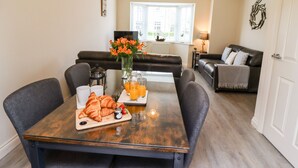 A dining area with a wooden table, two chairs, a vase with flowers, and a breakfast setting including croissants and orange juice. - Bay Cottage (Filey)