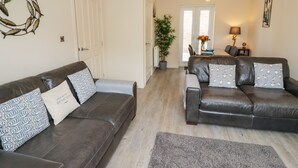 A living room with two leather sofas, a grey rug, a wooden floor, a white door, a potted plant, and a dining area with a table and chairs. - Bay Cottage (Filey)
