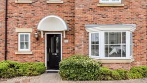 A brick building with a black door, a white archway entrance, and a bay window with white shutters. - Bay Cottage (Filey)