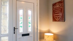 Uma porta branca com vitrais, uma luminária na parede e uma placa emoldurada acima da porta.