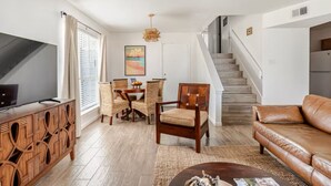 Una sala de estar moderna con televisor, mueble de madera, sofá de cuero y una escalera que sube a otro nivel.