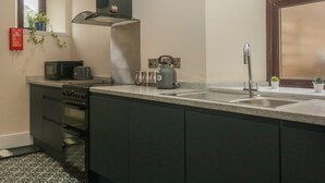 A modern kitchen with a stove, microwave, kettle, and sink. There is a window with a view of the outside, and a fire extinguisher on the wall. - Hillcrest (Newton Stewart)