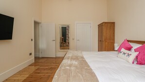 A bedroom with a large bed, wooden flooring, a wardrobe, a television, and a mirror. - Hillcrest (Newton Stewart)