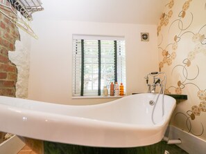 A bathroom with a freestanding bathtub, a window with blinds, and toiletries on a shelf. - The Hemmel (Faringdon)