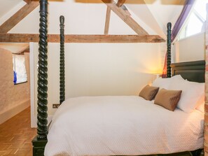 A bedroom with a four-poster bed, wooden beams, and a brick wall.