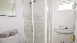 Un baño con inodoro, ducha con mampara de vidrio, lavamanos y espejo.