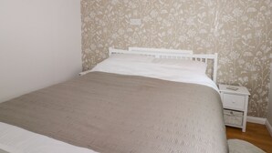 Un dormitorio con cama, mesita de noche blanca y papel tapiz floral.