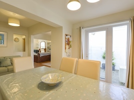 Un comedor con mesa, sillas y un cuenco decorativo. Se observa una cocina al fondo, un espejo y vistas al exterior.