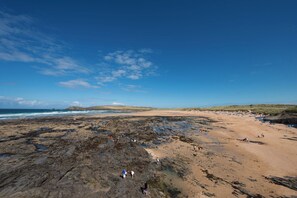 A coastal beach with rocky areas and sandy shores, people walking and relaxing. - Beachcomber (Padstow)