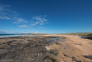 Una playa costera con zonas rocosas y orillas arenosas, gente caminando y descansando.