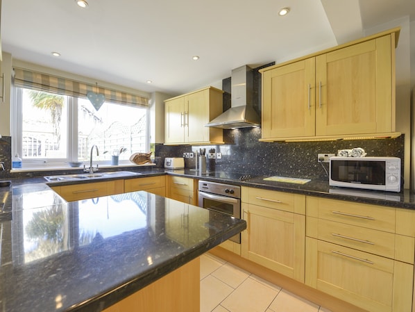 A modern kitchen with a large island, stainless steel appliances, and wooden cabinets. - Beachcomber (Padstow)