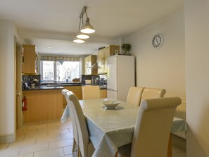 A compact kitchen with a dining area, featuring a table with chairs, a refrigerator, and a clock on the wall. - Beachcomber (Padstow)