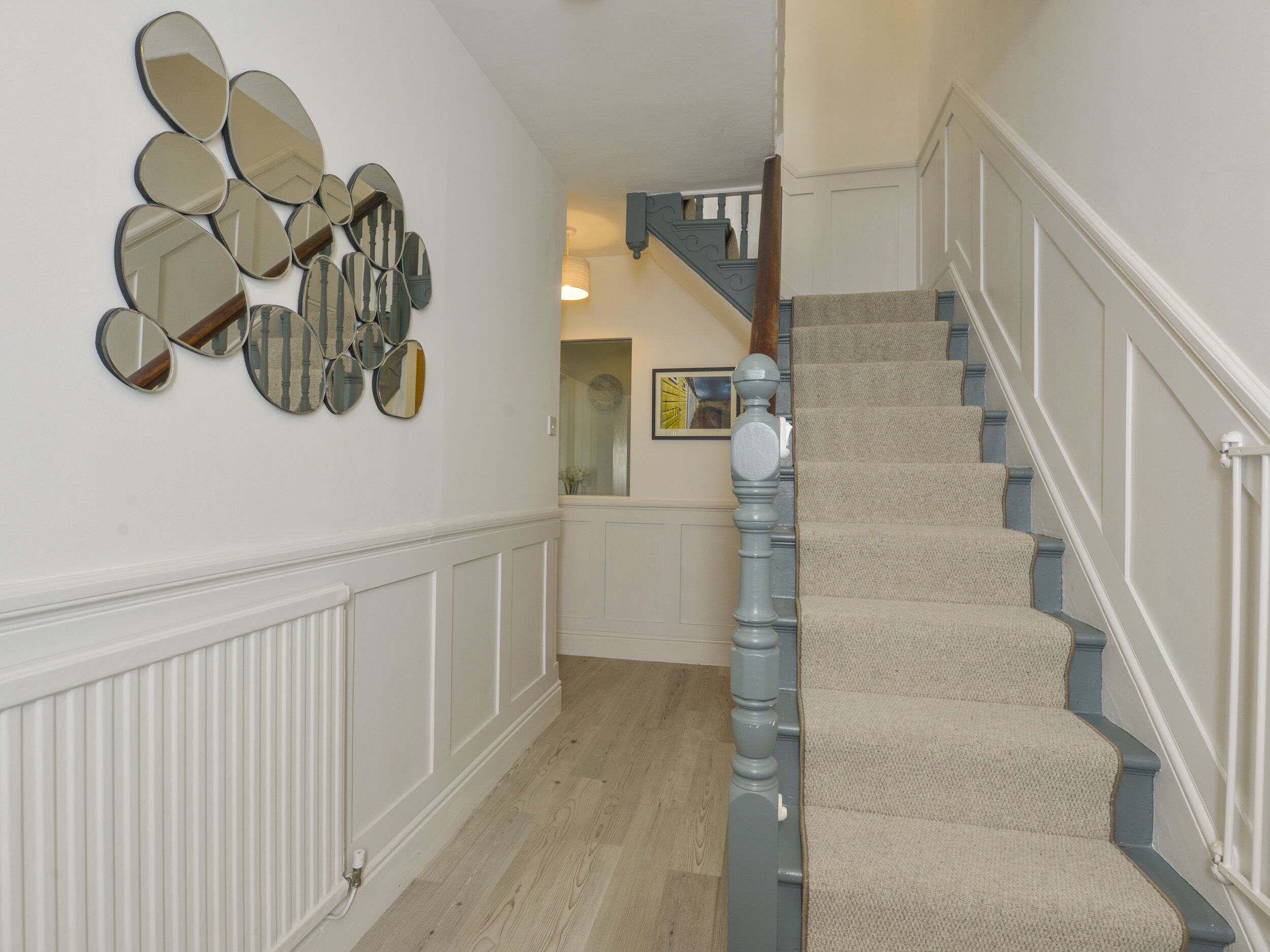A staircase with carpeted steps and a wooden handrail, leading to a landing with a white wall and a mirror arrangement.