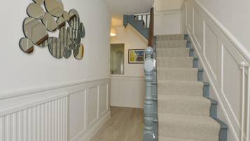 A staircase with carpeted steps and a wooden handrail, leading to a landing with a white wall and a mirror arrangement.