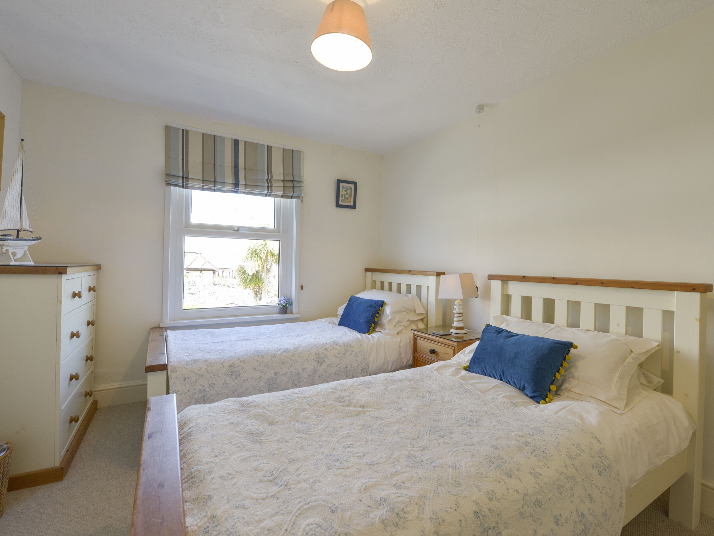 Une chambre avec deux lits simples, une commode, une fenêtre donnant sur un beau paysage et une lampe sur la table de chevet.