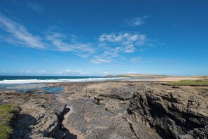 A rocky coastal landscape with a clear sky and ocean in the background. - Beachcomber (Padstow)