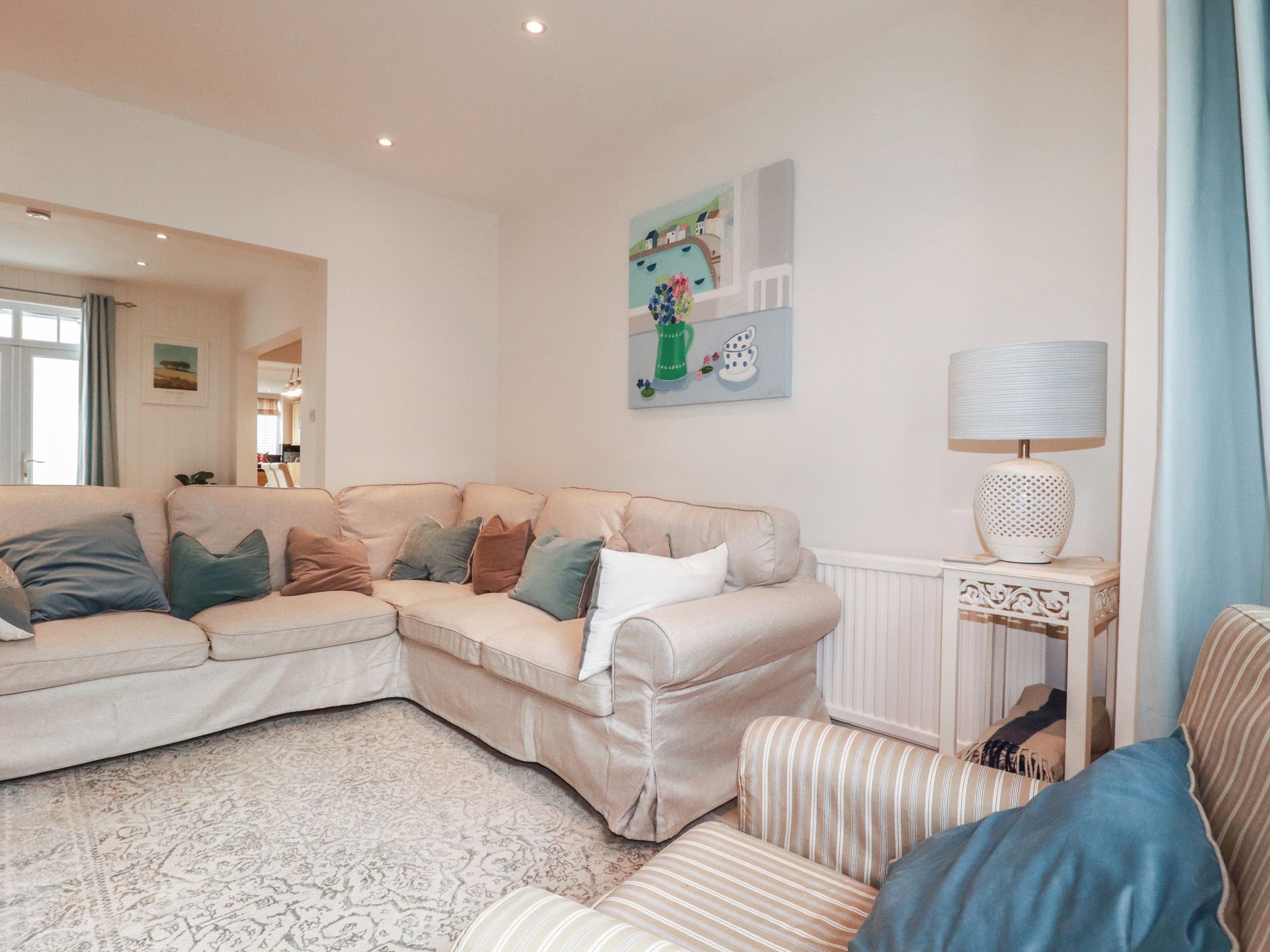 A living room with a beige sectional sofa, a patterned rug, and a painting on the wall.