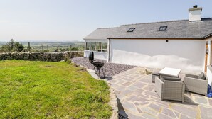 A house with a stone patio, outdoor furniture, and a view of the countryside. - Pen Y Braich Uchaf (Garndolbenmaen)