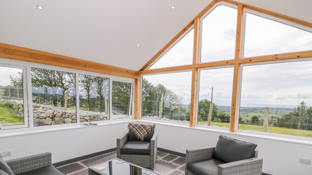 A modern room with large windows, wicker furniture, and a stone floor. - Pen Y Braich Uchaf (Garndolbenmaen)