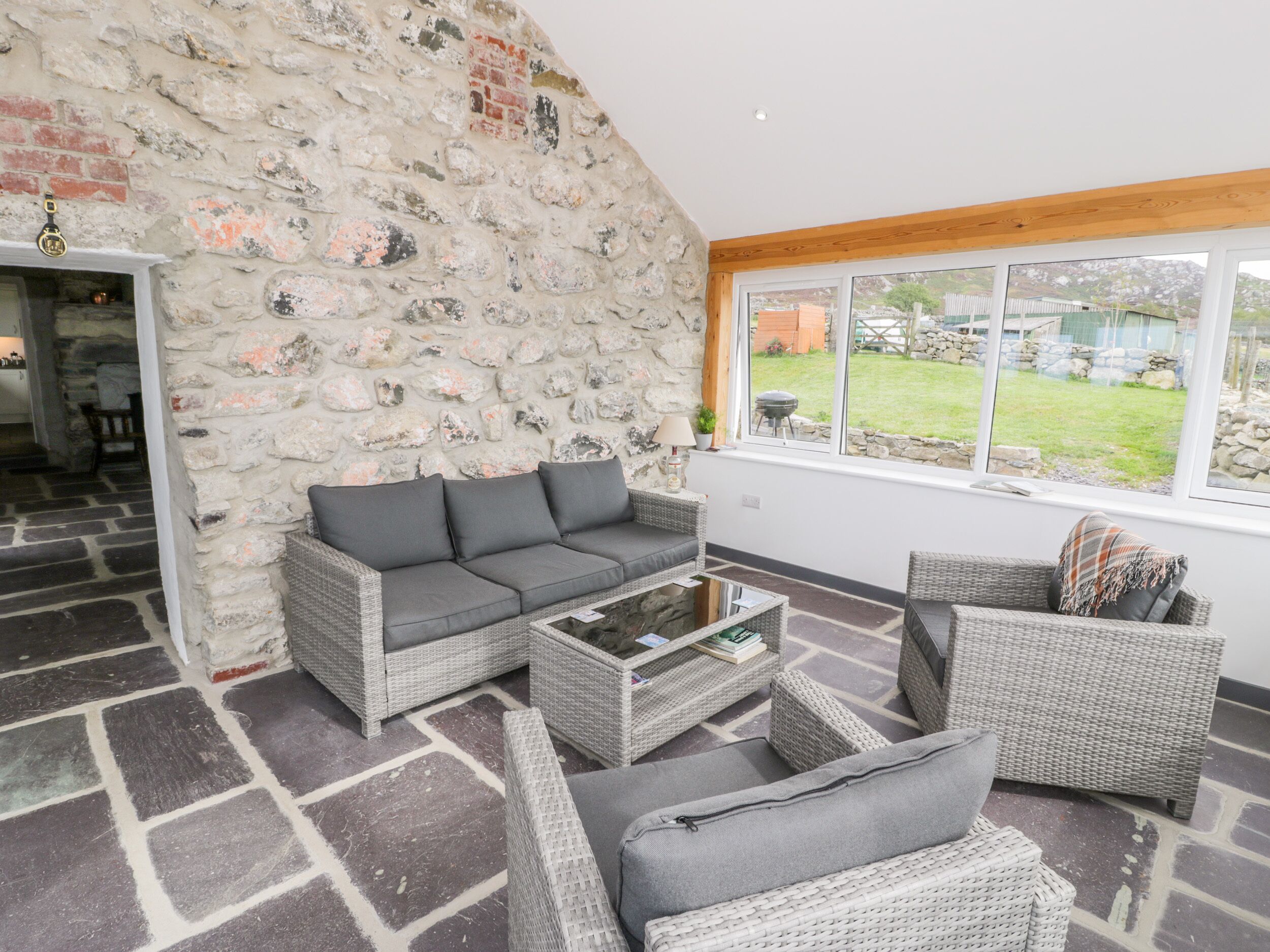 A cozy living room with a stone wall, wicker furniture, and a view of the garden.